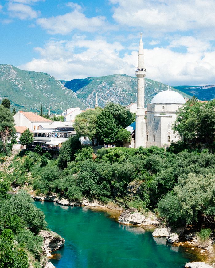 A stunning view of the Koski Mehmed Pasha Mosque in Mostar, surrounded by lush greenery and a serene river.