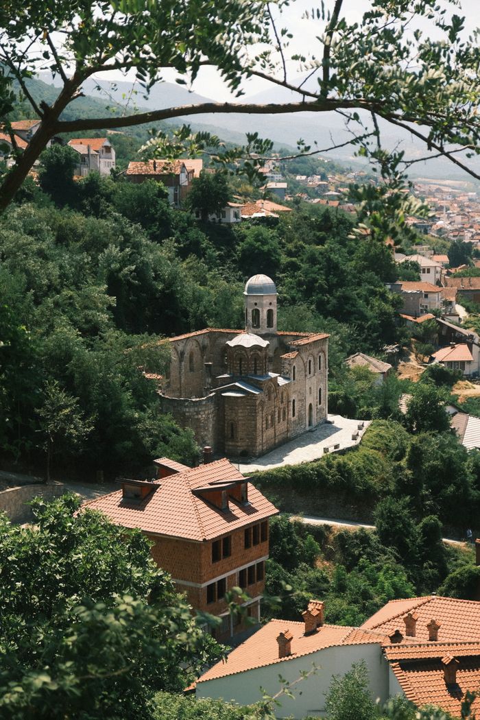 contact-img A picturesque view of a historic church in Prizren, Kosovo, amidst lush summer greenery.
